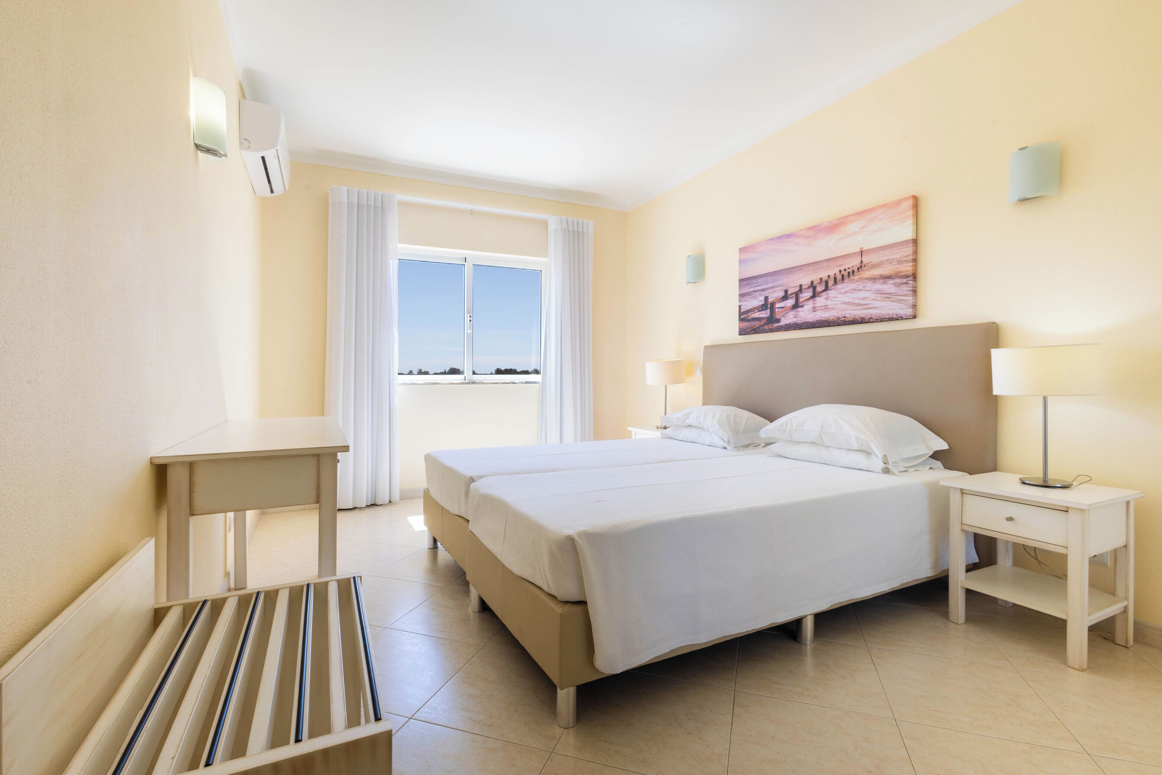 Una camera d'albergo con un letto grande, due comodini, una panca e una finestra con tende.