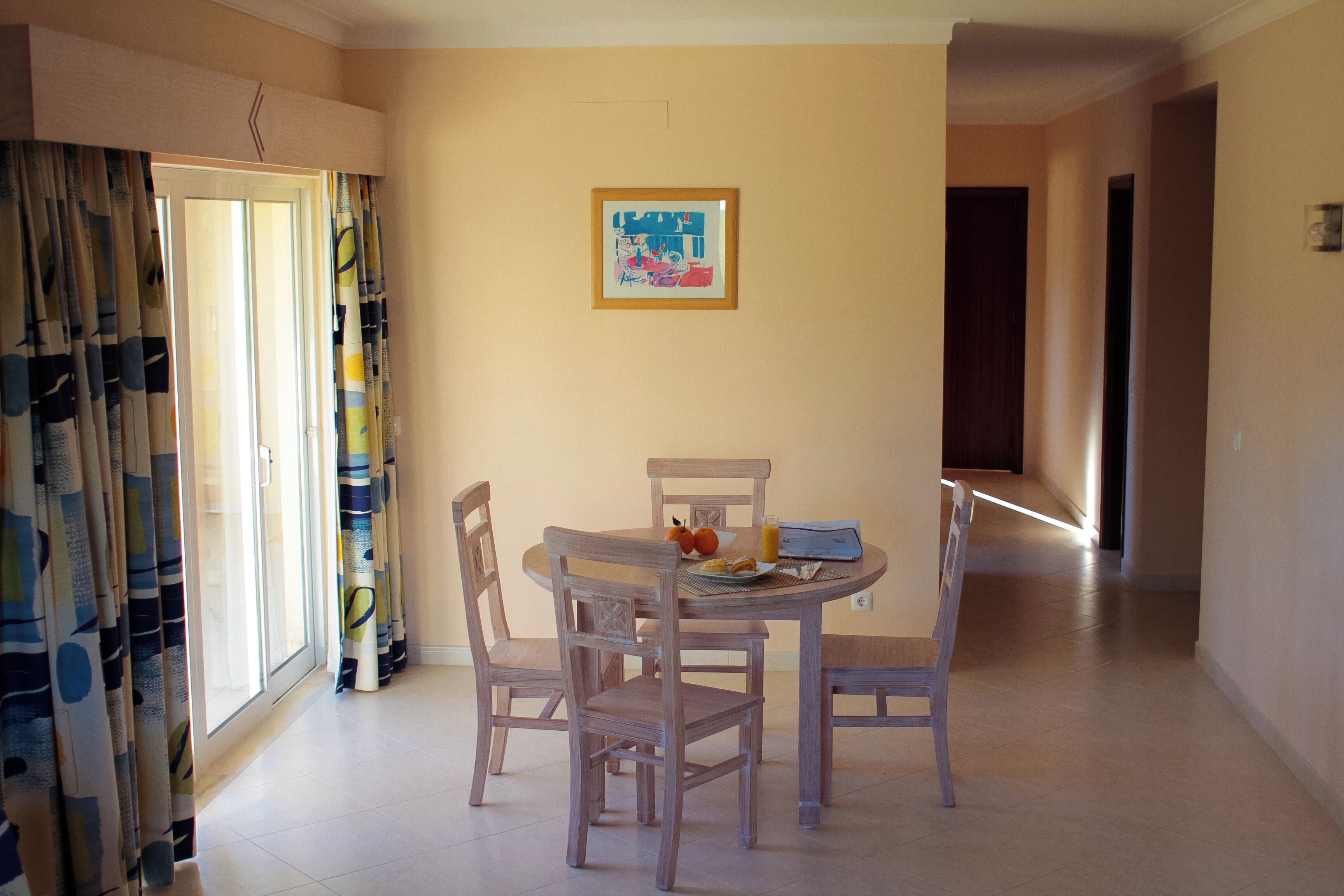 A dining area with a round table, four chairs, and a framed picture on the wall.
