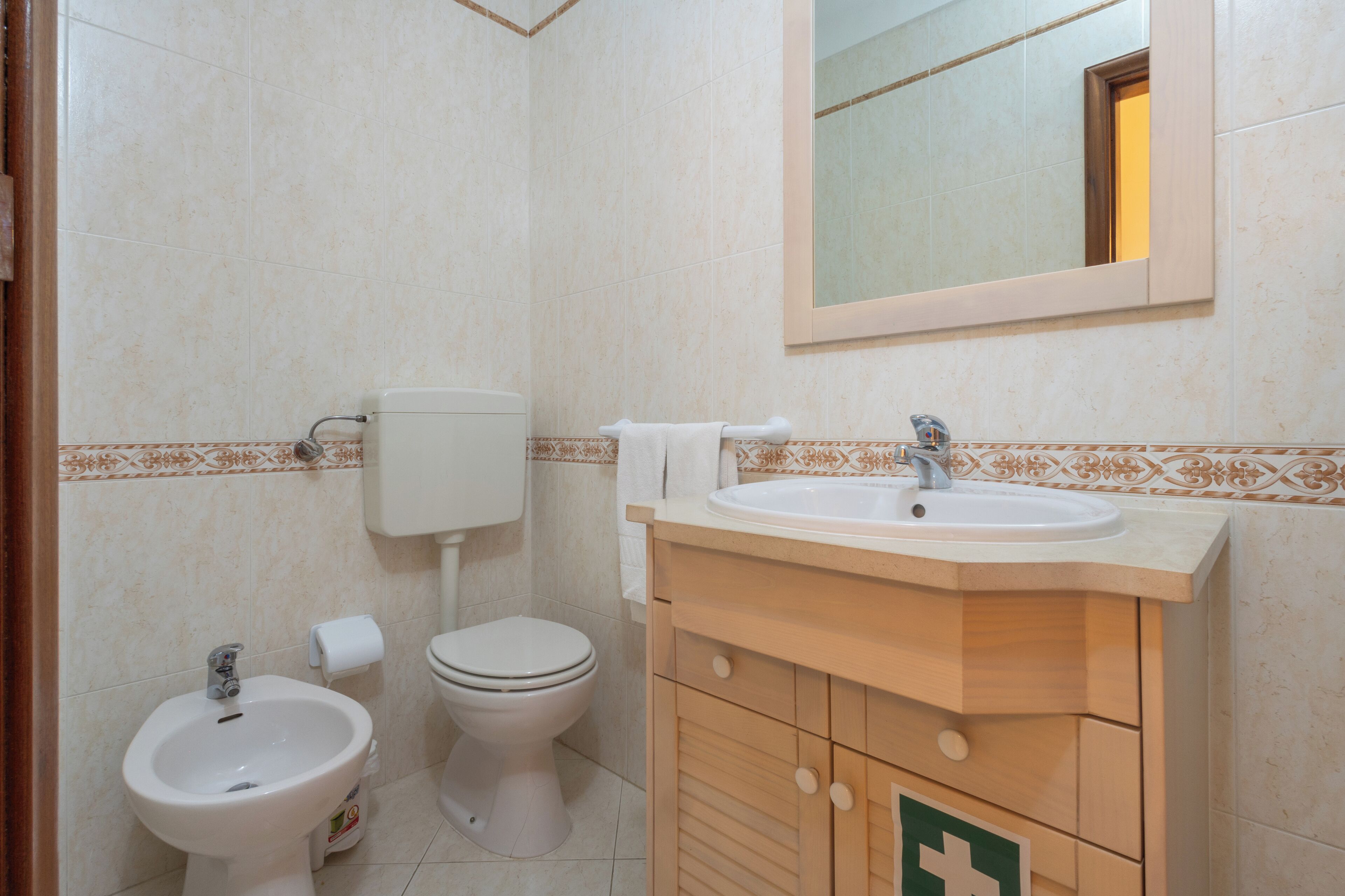 A bathroom with a toilet, bidet, sink, and mirror.