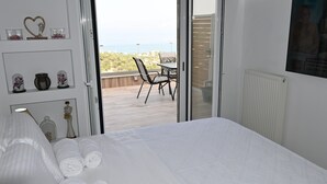 Une chambre avec un lit, des serviettes pliées, une table de chevet et une vue sur une terrasse extérieure avec une table et des chaises.