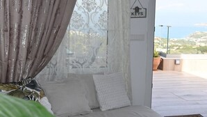Une chambre avec un lit, des rideaux blancs, une vue sur la mer et une pancarte sur laquelle on peut lire « CLÉS ».