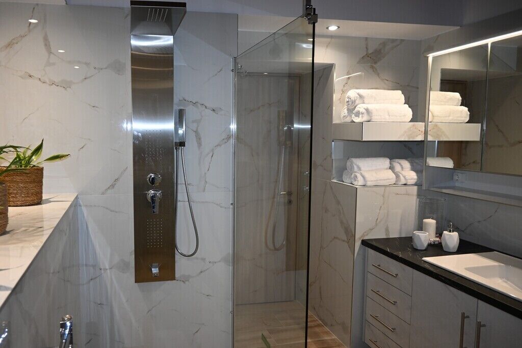Ein modernes Badezimmer mit einer gläsernen Dusche, Marmorwänden und einer schwarzen Arbeitsplatte.