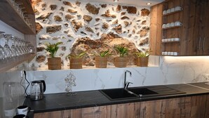Une cuisine avec un mur recouvert de pierres derrière l’évier, des armoires en bois, un plan de travail noir et un évier.