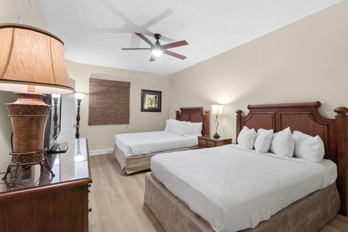 A hotel room with two beds, a ceiling fan, a lamp, and a picture on the wall.