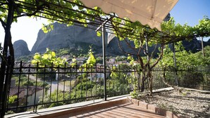A covered outdoor area with a metal fence, a pergola with vines, and a view of a town with buildings and mountains in the background.