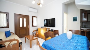A hotel room with a bed, a sofa, a wooden table, a TV, and a kitchenette.