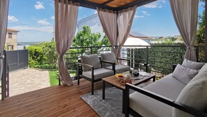 Ein Balkon mit Holzboden, zwei Sofas, einem Tisch mit Obstschale und Blick auf Grünflächen und Gebäude.