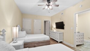 A bedroom with two beds, a ceiling fan, a dresser, and a TV. - Beachfront Paradise: Spacious 2BR Condo with Views (North Myrtle Beach)