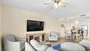 A spacious living room with a large flat-screen TV, a ceiling fan, and a dining area with a kitchen in the background. - Beachfront Paradise: Spacious 2BR Condo with Views (North Myrtle Beach)