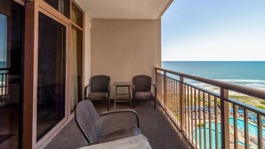 Uma varanda com duas cadeiras de vime, uma mesa pequena e vista para o oceano e área da piscina.
