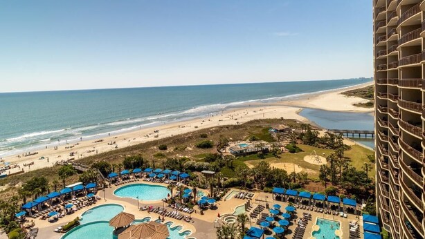 Um resort com várias piscinas, uma praia e um edifício alto.