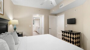 A hotel room with a bed, a nightstand with a lamp, a dresser, and a television on the wall.