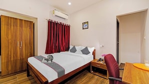 Een hotelkamer met een bed, een houten kledingkast, een bureau met stoel, een nachtkastje en een airconditioning.