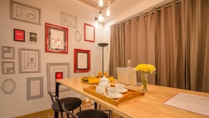 Een eetgedeelte met een houten tafel gedekt voor het ontbijt, foto's aan de muur en uitzicht buiten door gordijnen.