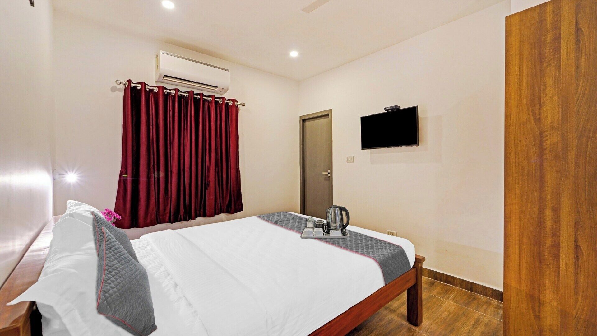 Ein Hotelzimmer mit Bett, Nachttisch, Klimaanlage, Fernseher und Holztür.