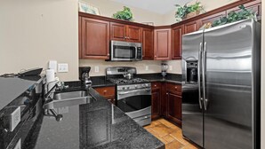 A modern kitchen with stainless steel appliances, dark wooden cabinets, and a granite countertop. - Oceanfront Oasis: 2BR 2BA Condo with Stunning Views (North Myrtle Beach)