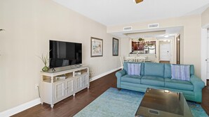 A living room with a flat-screen TV, a teal sofa, and a ceiling fan. - Oceanfront Oasis: 2BR 2BA Condo with Stunning Views (North Myrtle Beach)