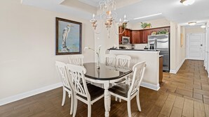 A dining area with a round table and white chairs, a chandelier, and a kitchen in the background. - Oceanfront Oasis: 2BR 2BA Condo with Stunning Views (North Myrtle Beach)