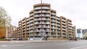 Ein mehrgeschossiges Wohngebäude mit Balkonen, einer Bushaltestelle und einer Fußgängerampel.