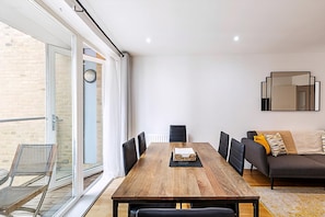 A modern living room with a wooden dining table, black chairs, a sofa, and a large mirror.