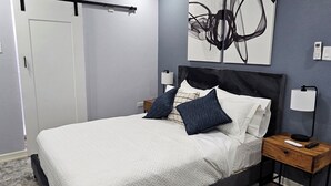 A modern bedroom with a bed, a ceiling fan, a wall-mounted air conditioner, and a bedside table with a lamp.