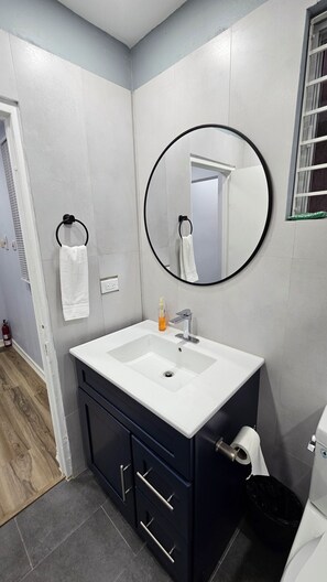 Un baño con lavamanos blanco, armarios oscuros, un espejo redondo y una toalla colgada en un perchero.