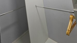 A corner of a room with a white door, a metal rod, and a wooden hanger.