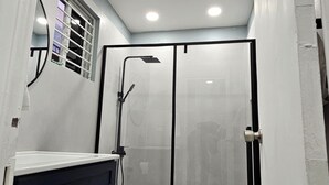 A modern bathroom with a glass shower enclosure, a white toilet, and dark blue cabinets.