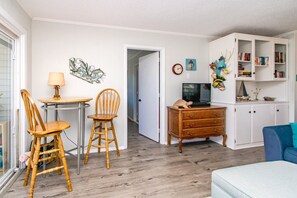 Un salon avec une table en bois, deux chaises, un téléviseur, une bibliothèque et un canapé bleu.