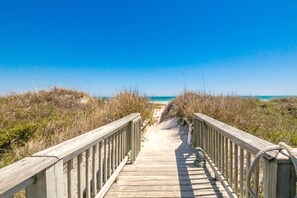 Une promenade en bois qui mène à une plage, sous un ciel dégagé.