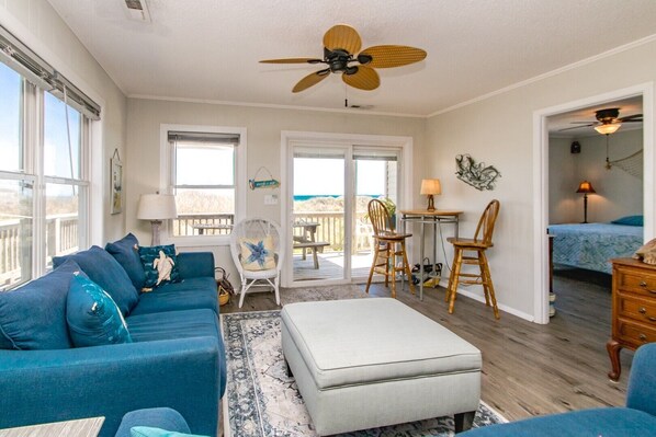 A spacious living room with a blue sofa, a white ottoman, and a ceiling fan.