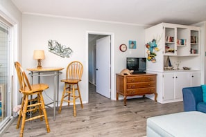 Un salon avec un canapé, un coin repas avec des chaises et une table, un téléviseur et une bibliothèque.