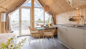 Een knus vakantiehuisje met een grote glazen deur die uitkijkt op het strand, een houten interieur en een eethoek met rieten stoelen.