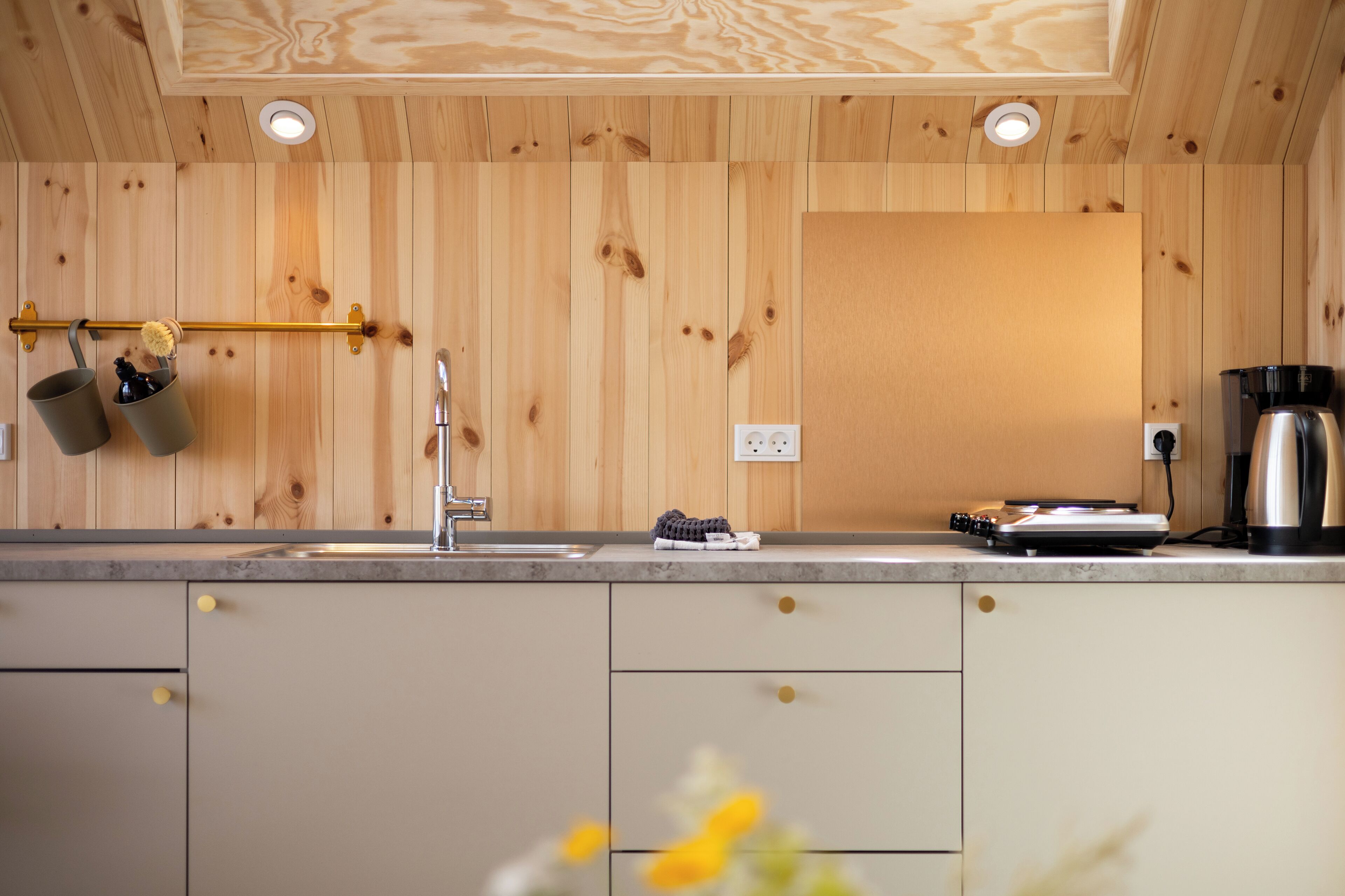 Une cuisine avec des murs recouverts de panneaux en bois, un évier en acier inoxydable, une machine à café et une bouilloire posées sur le plan de travail.