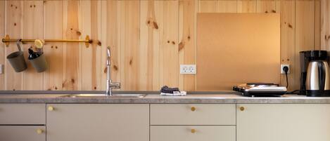 A kitchen with wooden panel walls, a stainless steel sink, a coffee maker, and a kettle on the counter.