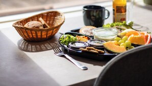 Een ontbijfwagen met brood, fruit en toevoegingen op een tafel bij een raam met uitzicht op een veld.