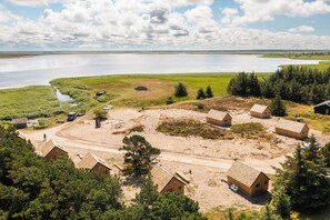 A remote cabin area with several wooden cabins, a dirt road, and a body of water in the background. - Bilberghus - Beyond Bed & Breakfast (Hvide Sande)