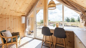 Een gezellig cabin interieur met houten wanden, een eethoek met twee stoelen, een hanglamp van riet en een groot raam met uitzicht op de natuur.