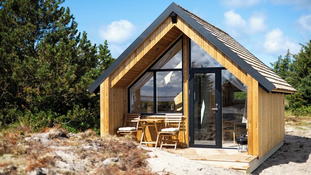 Een houten hut met grote ramen, een eethoek en een klein terras.
