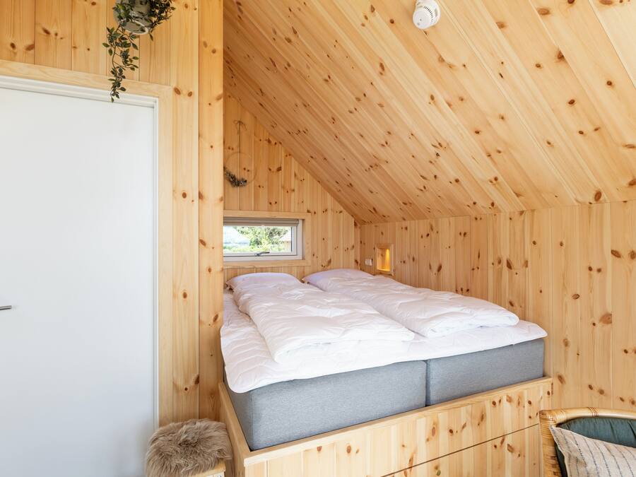 A wooden room with a bed, a window, and a door.
