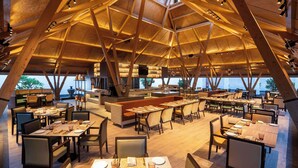 An interior with a high ceiling and wooden beams, featuring tables and chairs arranged for dining. - Radisson Resort Hatgad Saputara (Surgana)