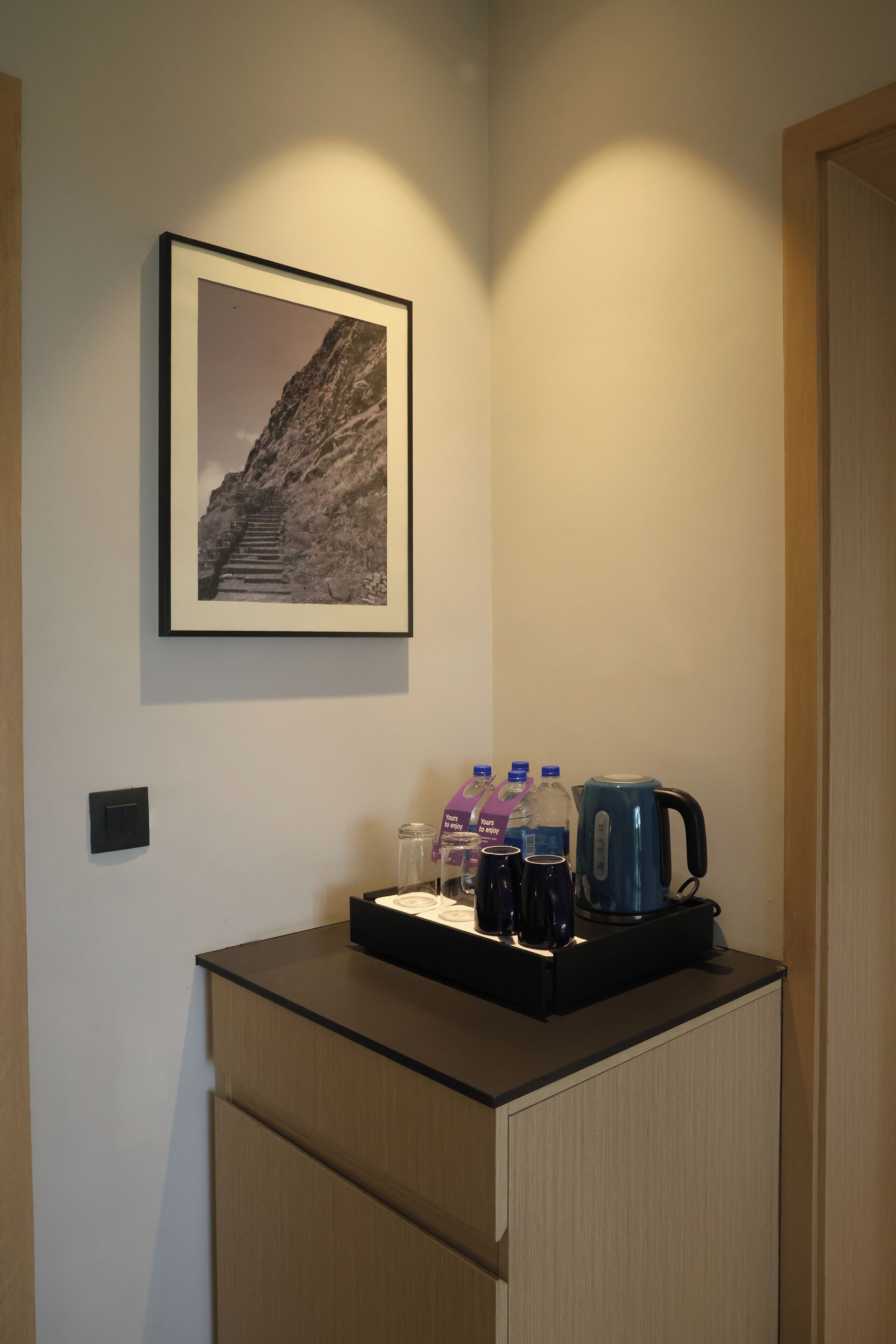 A small kitchenette with a coffee maker, water bottles, and a framed picture of a mountain on the wall.