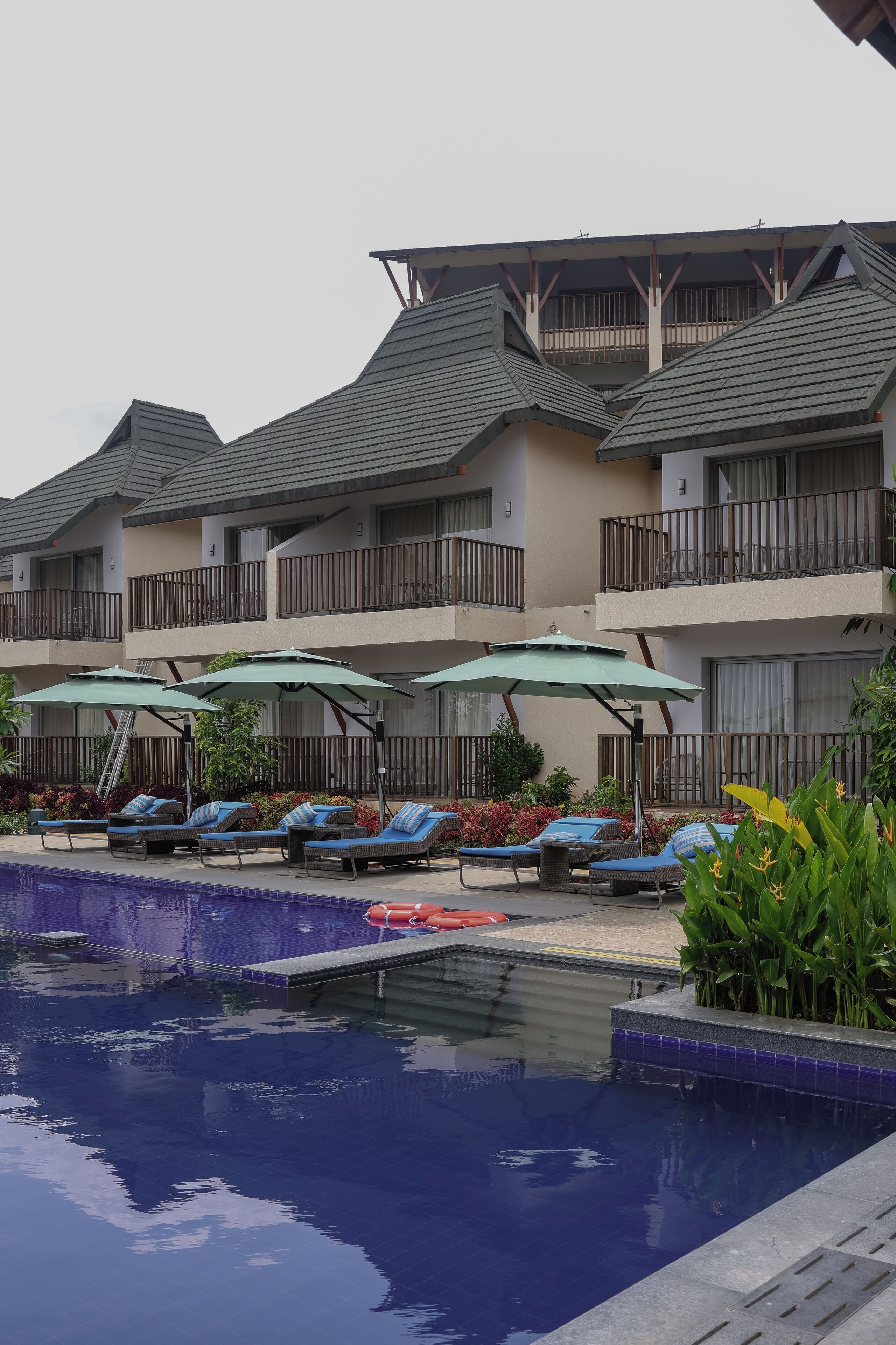 A hotel with a swimming pool, lounge chairs, and umbrellas.