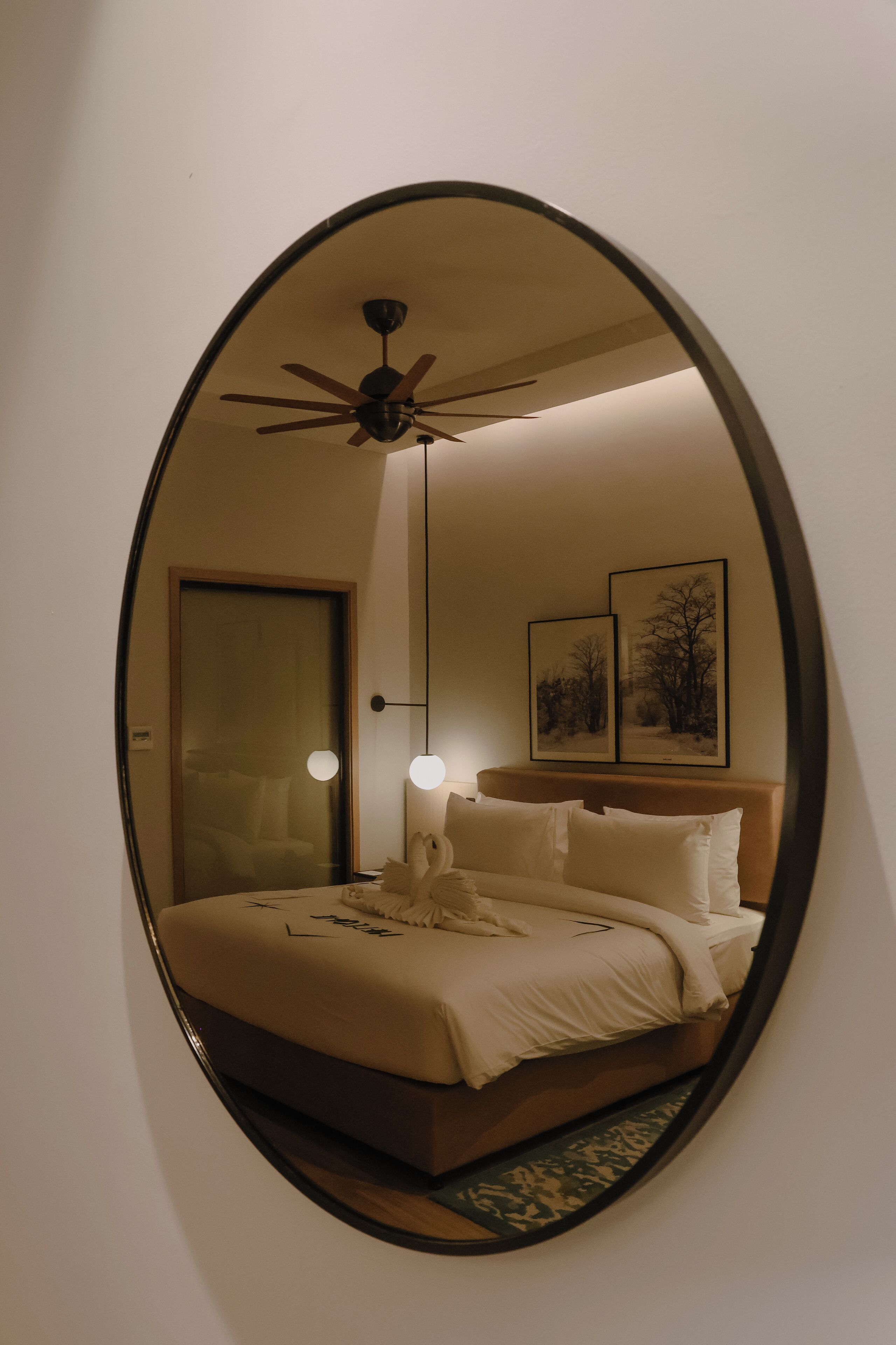 Une chambre à coucher comprenant un lit, un ventilateur de plafond, deux lampes fixées au mur et deux tableaux encadrés.