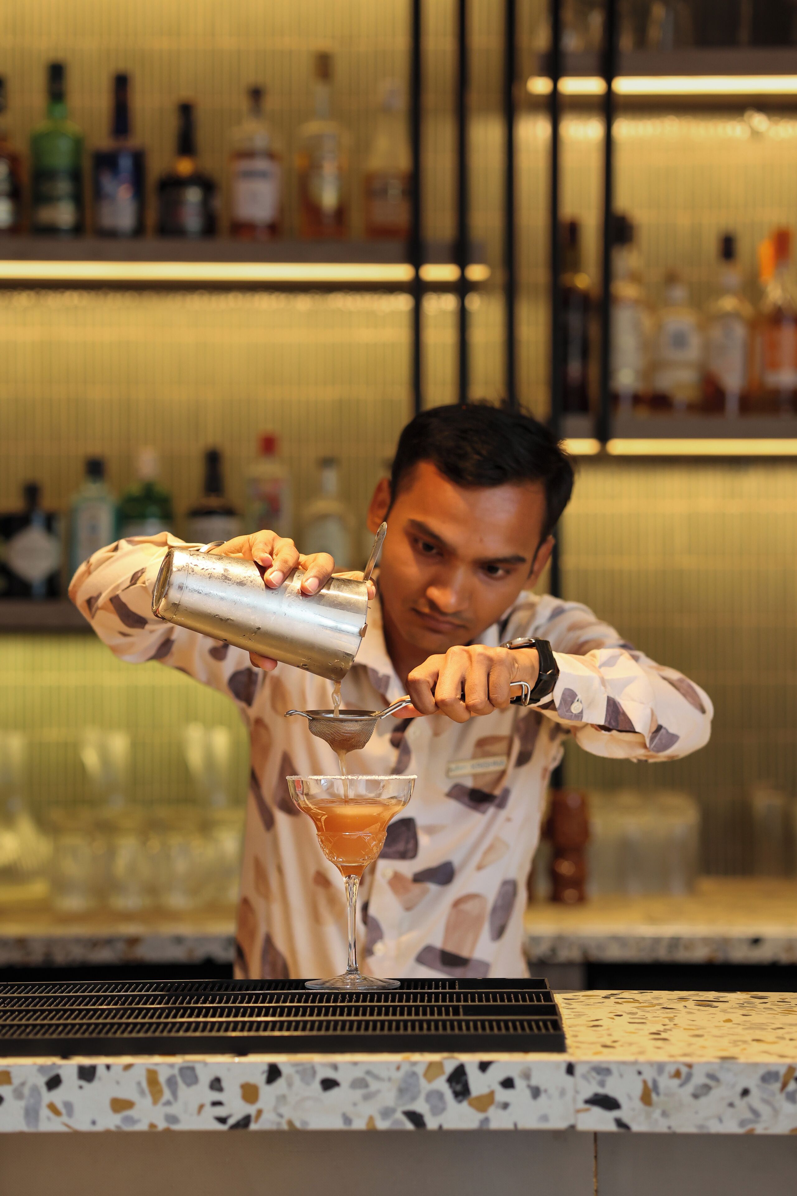 Ein Barkeeper gießt ein Getränk in ein Martini-Glas.