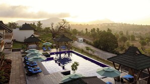 A pool area with lounge chairs and umbrellas, surrounded by a landscaped garden and a view of distant mountains. - Radisson Resort Hatgad Saputara (Surgana)