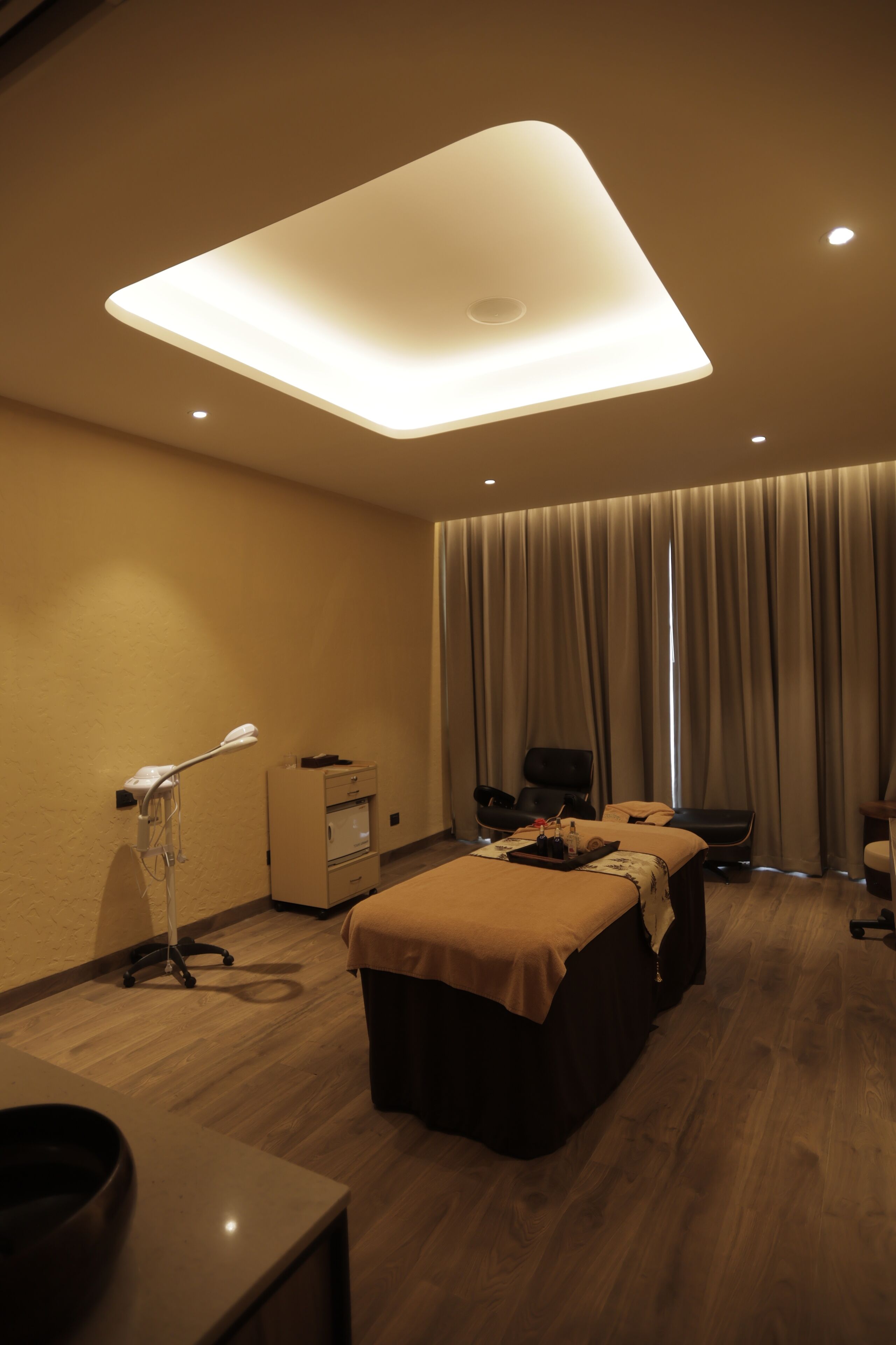 A hotel room with a large bed, a desk, a chair, a massage table, and a ceiling light fixture.