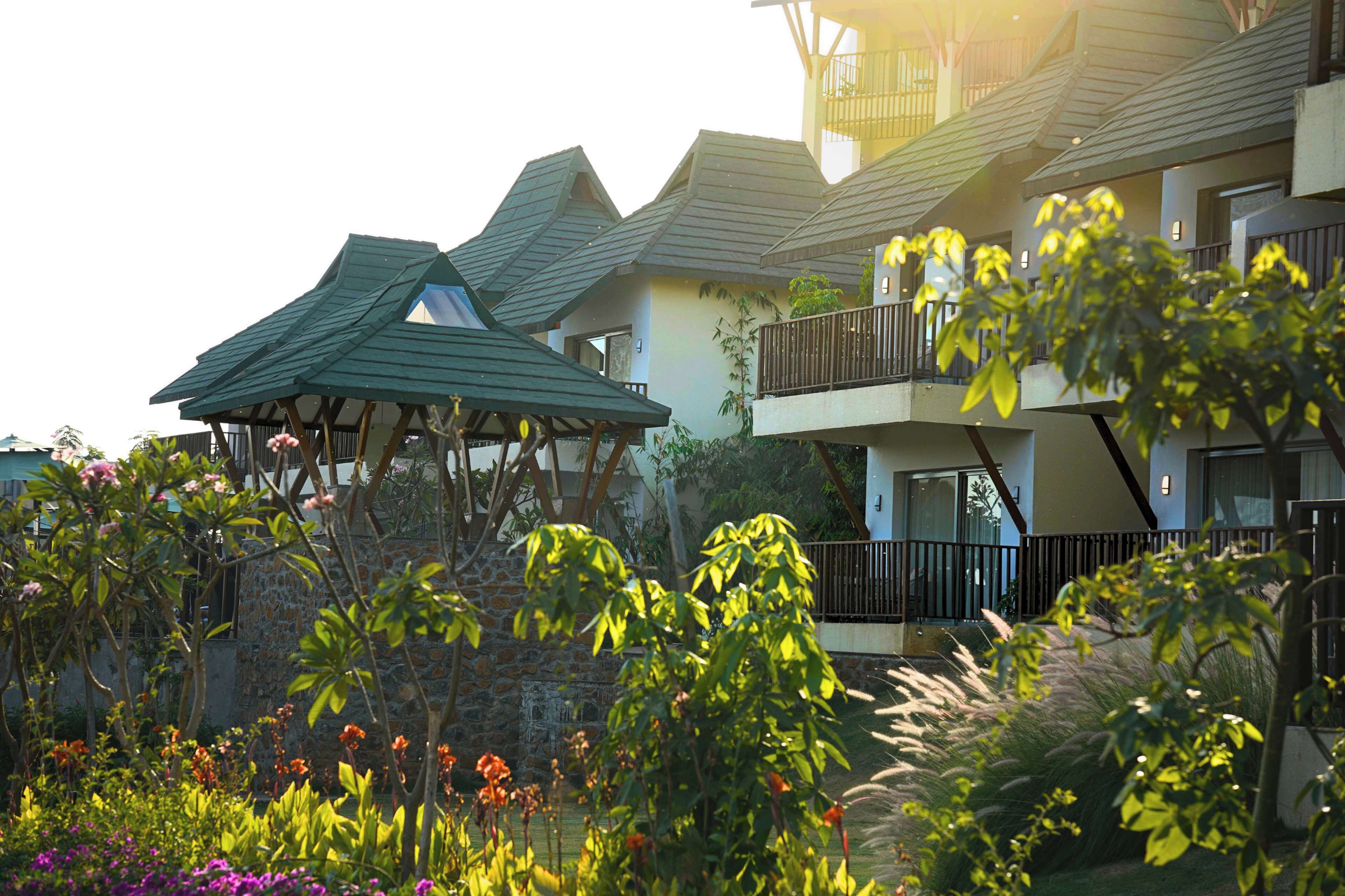 Um hotel com vários edifícios, um gazebo e um jardim com diversas plantas e flores.
