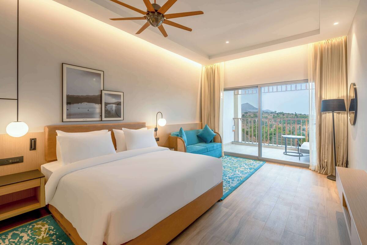 Quarto de hotel com cama grande, ventoinha no teto, varanda com vista e uma janela ampla.