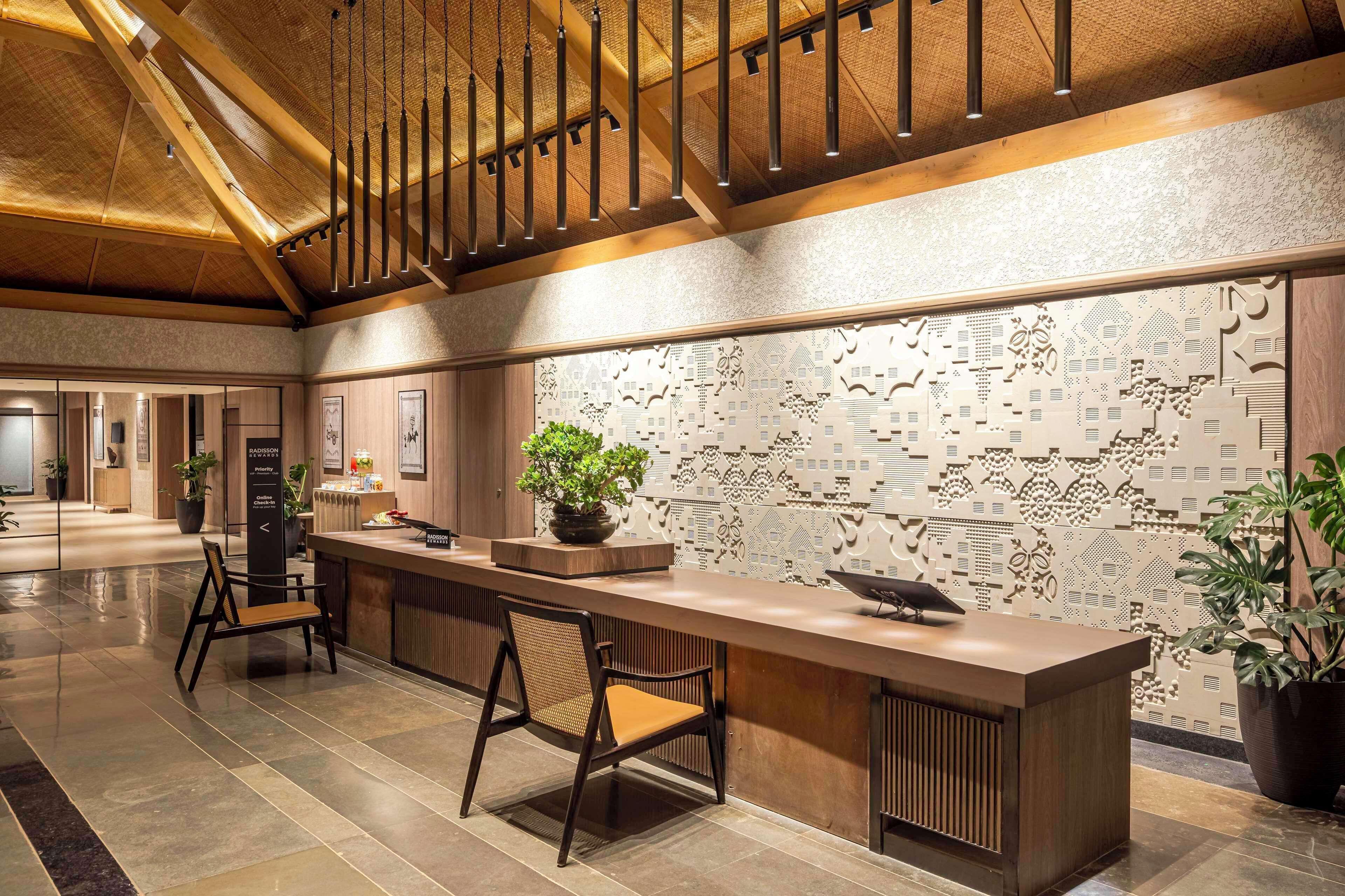 A reception area with a wooden reception desk, a potted plant, and a patterned wall.